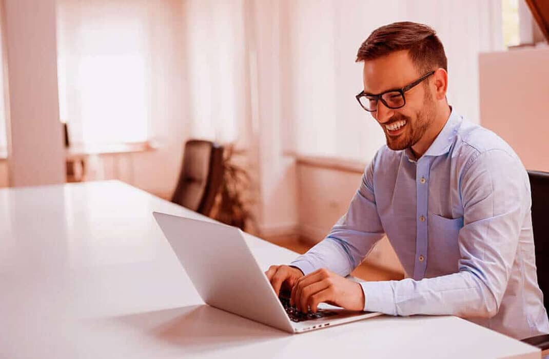 a man smiling and working on his laptop
